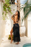 Mujer posando junto a palmera, con bikini y falda larga color negro